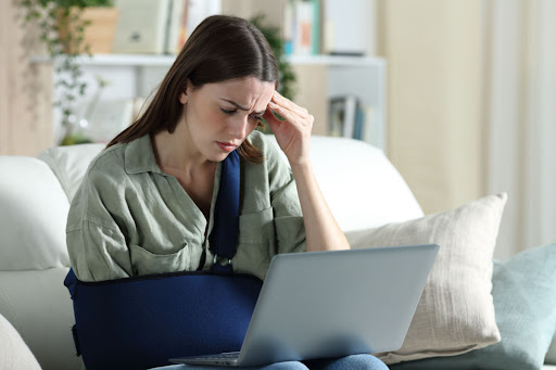 a woman with a broken arm sits frowning on a couch with her laptop